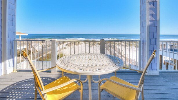 A covered outdoor seating area with a table and chairs, overlooking a beach. - Sea Monster, West. Big. Beachfront. Pool. Sleeps 26. Awesome location! (Gulf Shores)