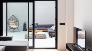 A modern living room with a sofa, a chair, a television, and a sliding glass door leading to a balcony.