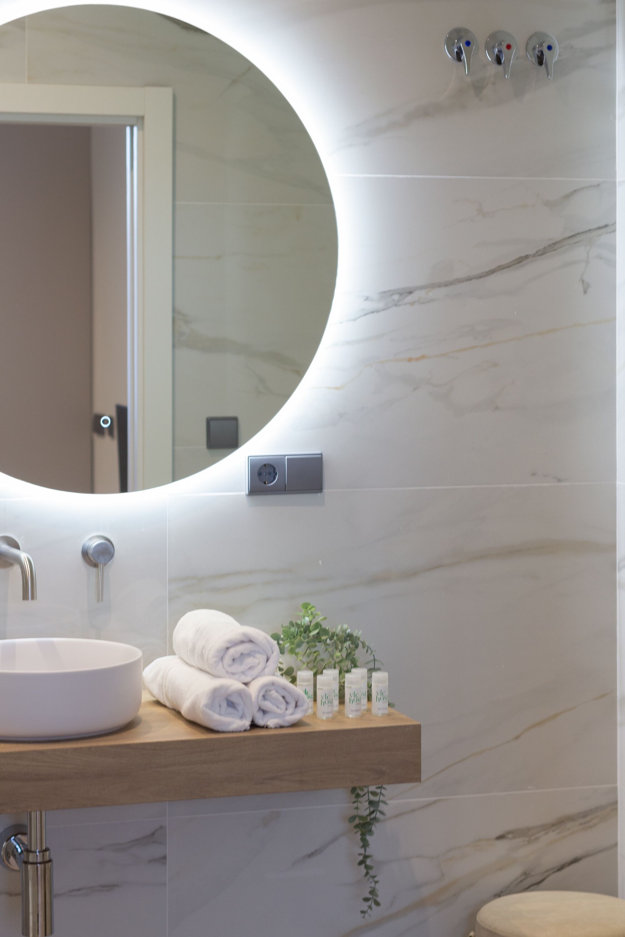 A bathroom with a round mirror, a sink, and a wooden shelf with towels and toiletries.