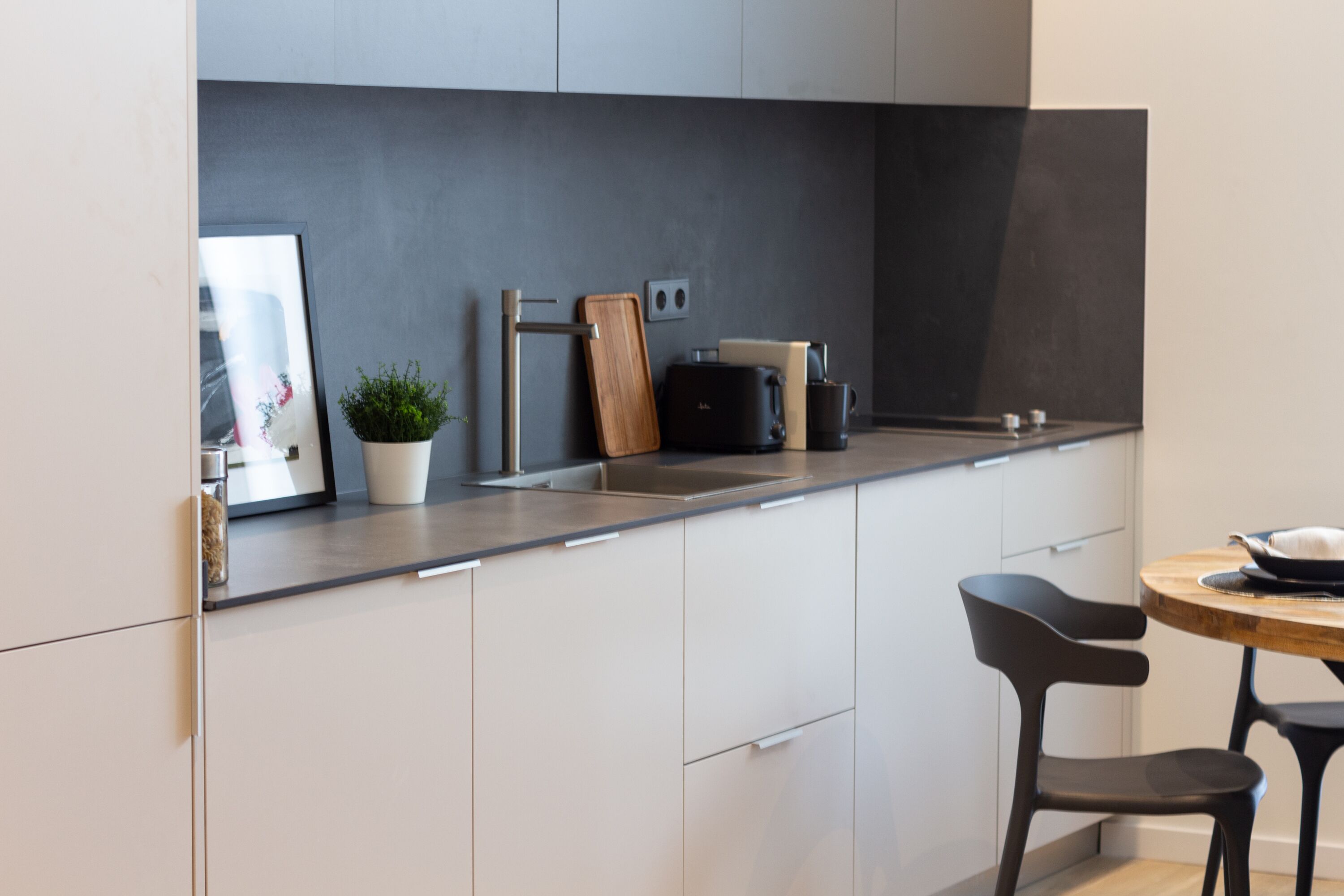 A modern kitchen with white cabinets, a stainless steel sink, a black coffee machine, and a wooden cutting board.