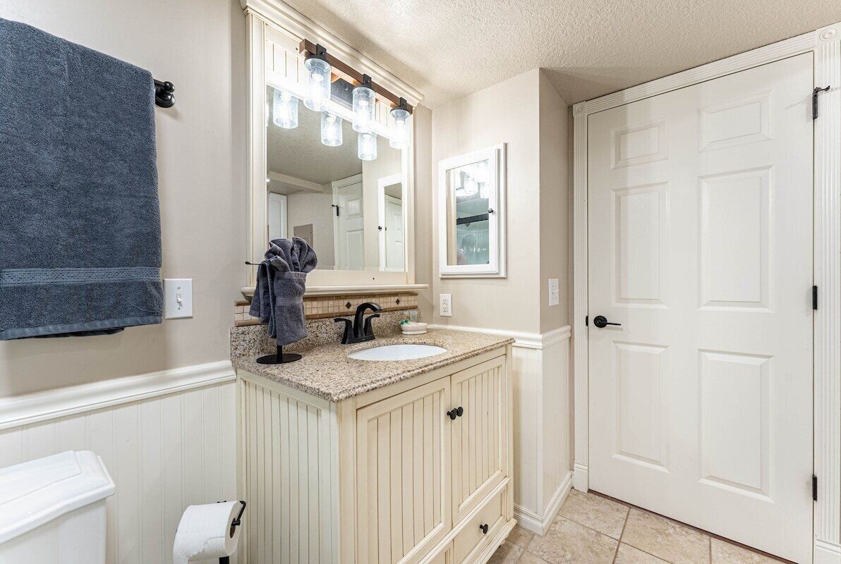 Une salle de bain avec un meuble-lavabo beige, un lavabo blanc, un miroir avec éclairage intégré, un porte-serviettes et une porte blanche.