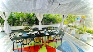 Un espacio comedor al aire libre cubierto, con una mesa dispuesta para cuatro personas, rodeada de sillas y un suelo de baldosas de colores.