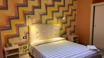 Habitación de hotel con cama, mesita de noche, teléfono y una pared con diseño en zigzag.