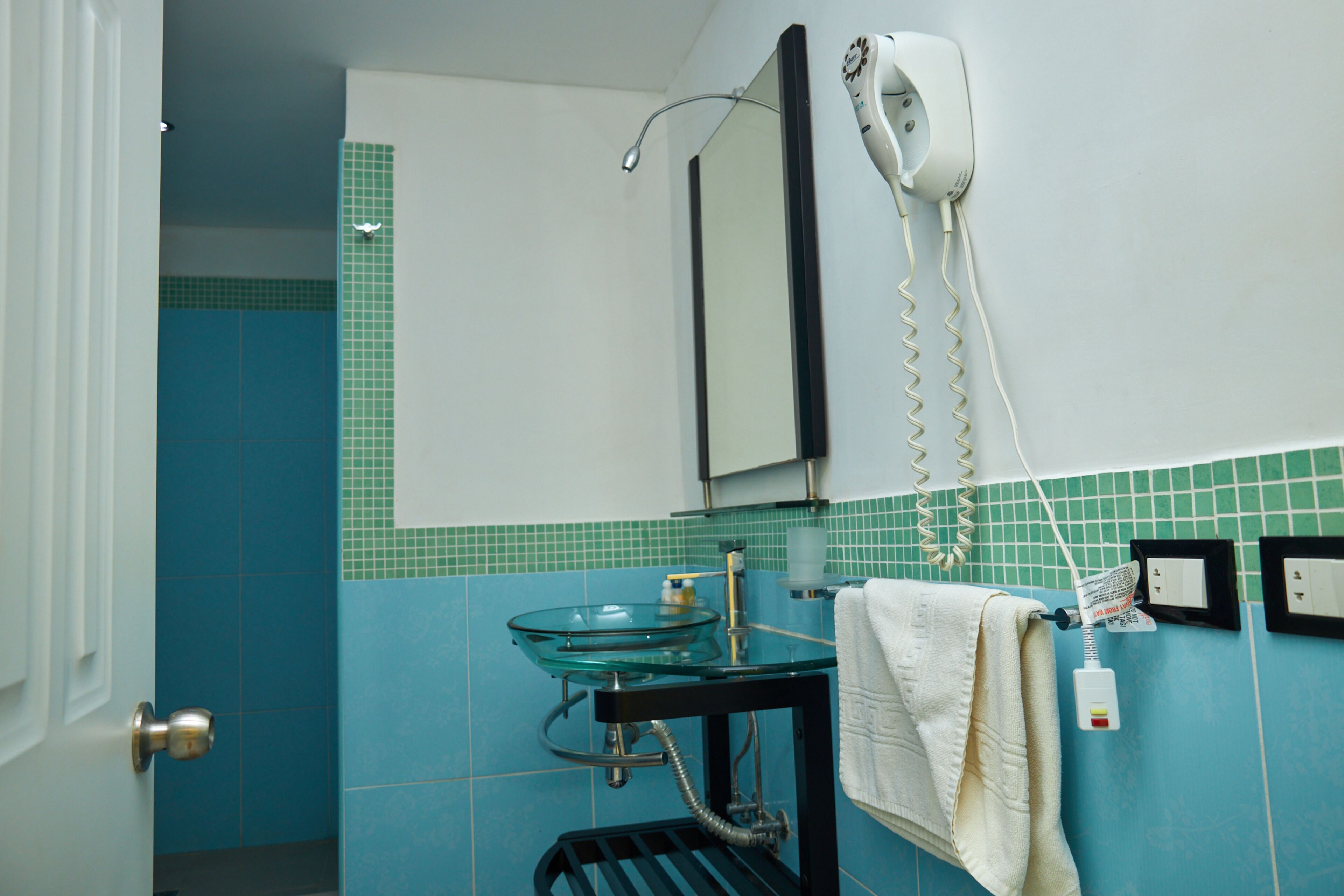 A bathroom with a glass sink, a hairdryer, and a towel hanging on the wall.