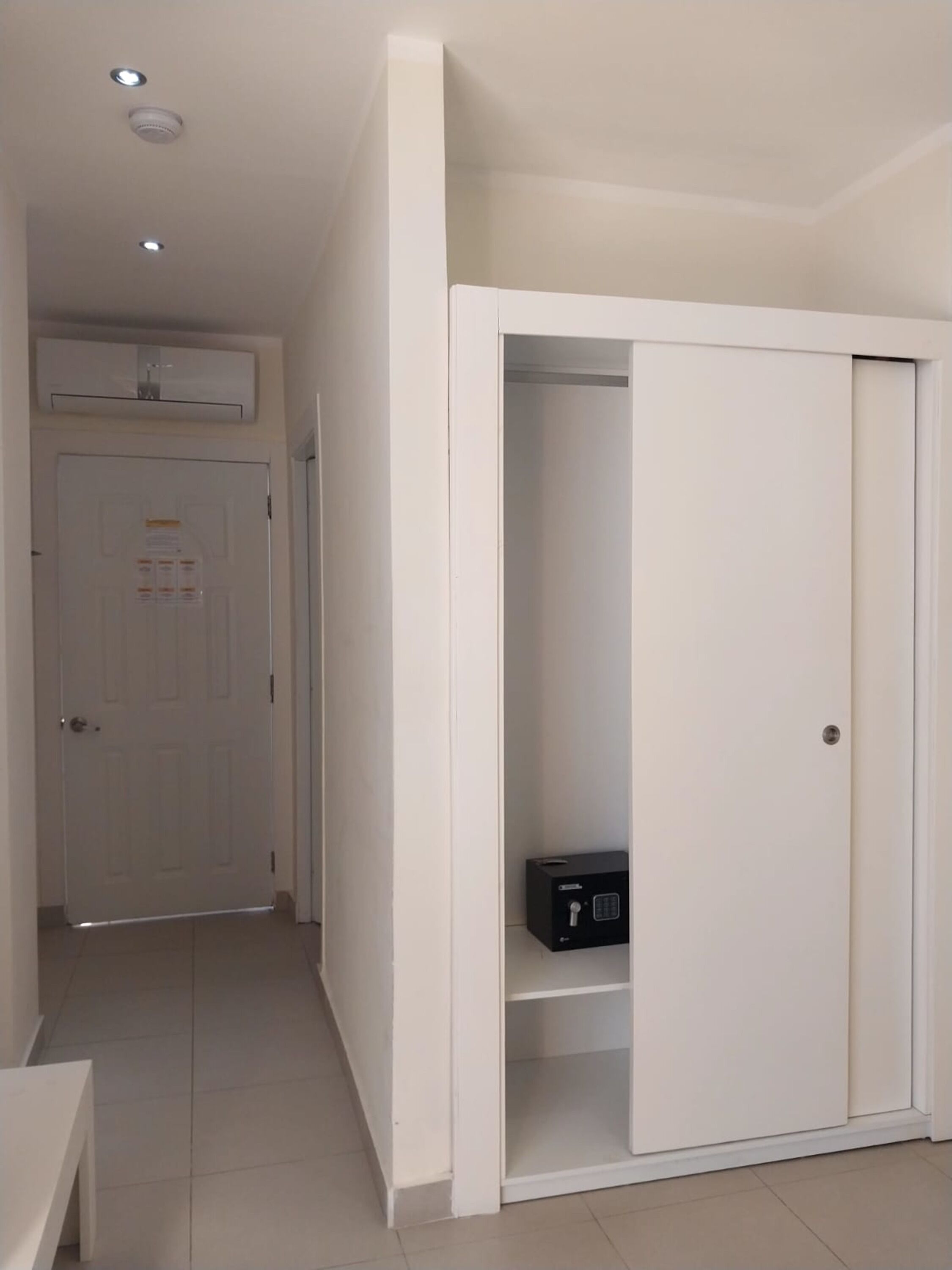 A hallway with a white door, a white wardrobe, and a small black object on the lower shelf.