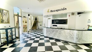 Zona de recepción con piso a cuadros, un mostrador de recepción y una escalera que sube a otro nivel.