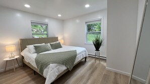 A modern bedroom with a large bed, two bedside tables with lamps, and a potted plant.