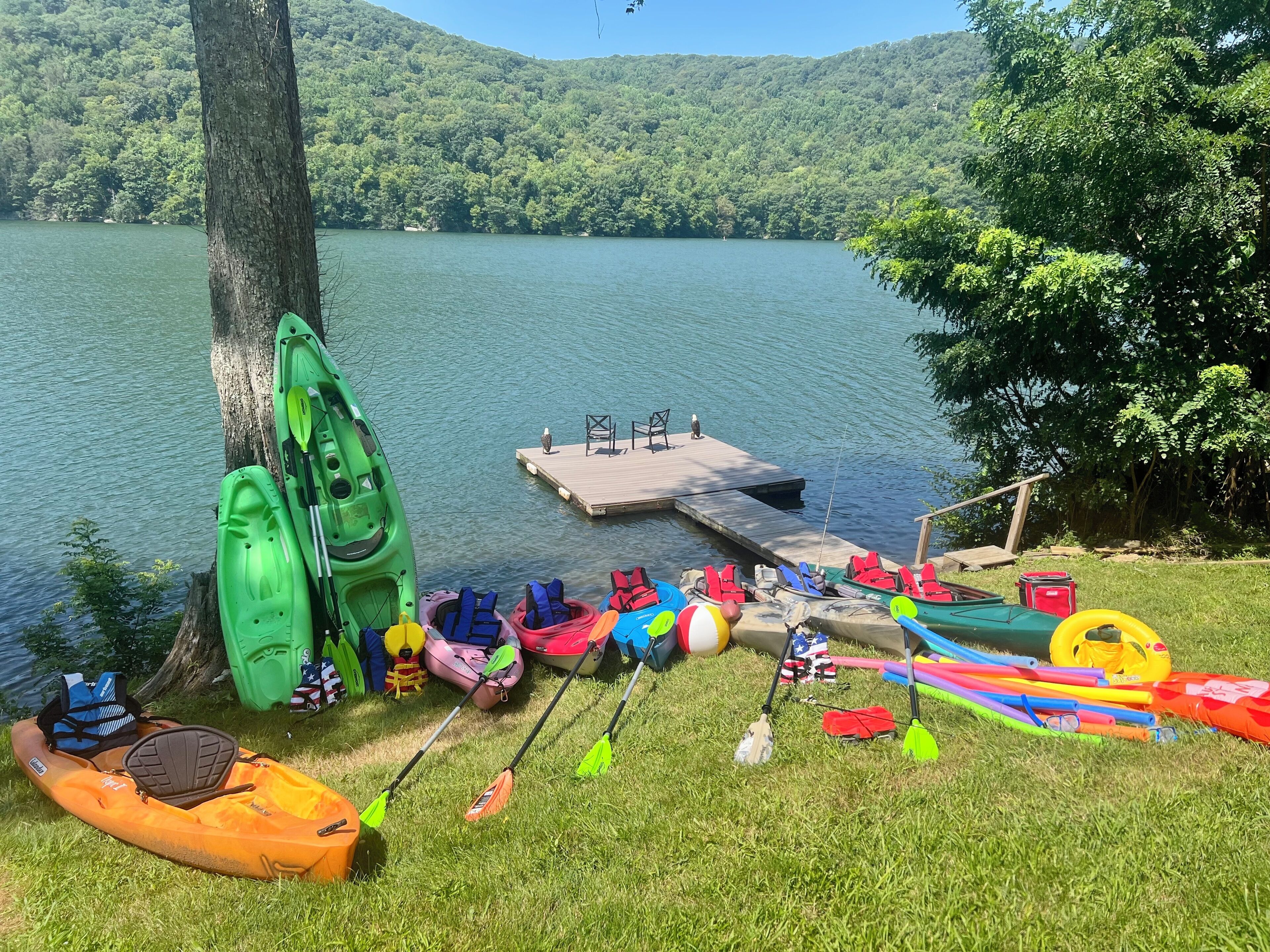 A lakeside scene with kayaks, paddleboards, and life jackets near a dock.