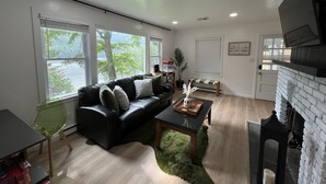A modern living room with a black leather sofa, a green rug, and a fireplace.