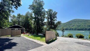 A lakeside cabin with a covered patio, surrounded by trees and a view of a lake and hills.