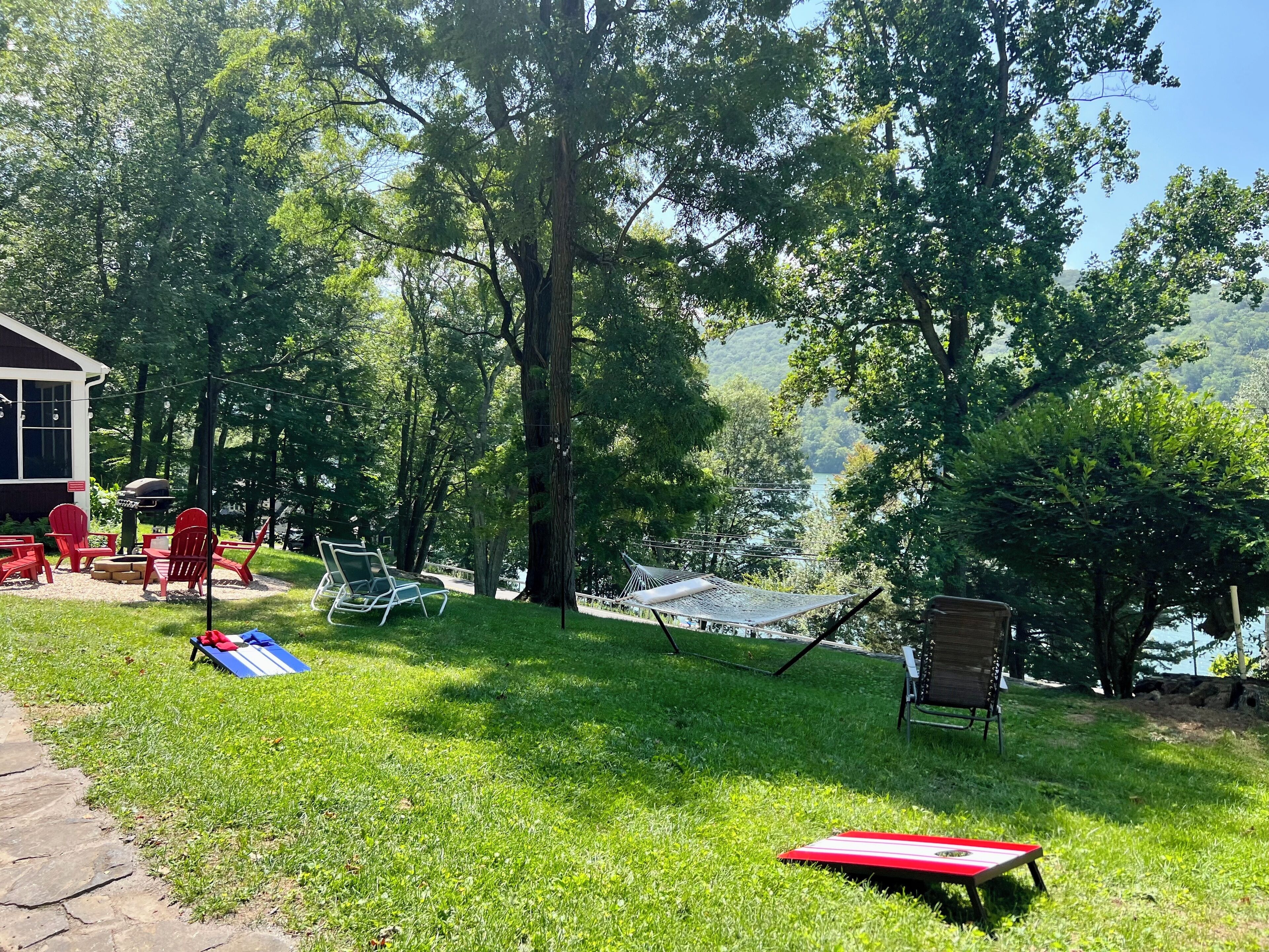 Ein Garten mit einer Hängematte, roten Stühlen, einem Grill und Blick auf einen See.