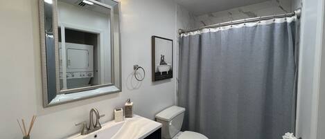 A bathroom with a vanity, sink, mirror, toilet, and shower curtain.