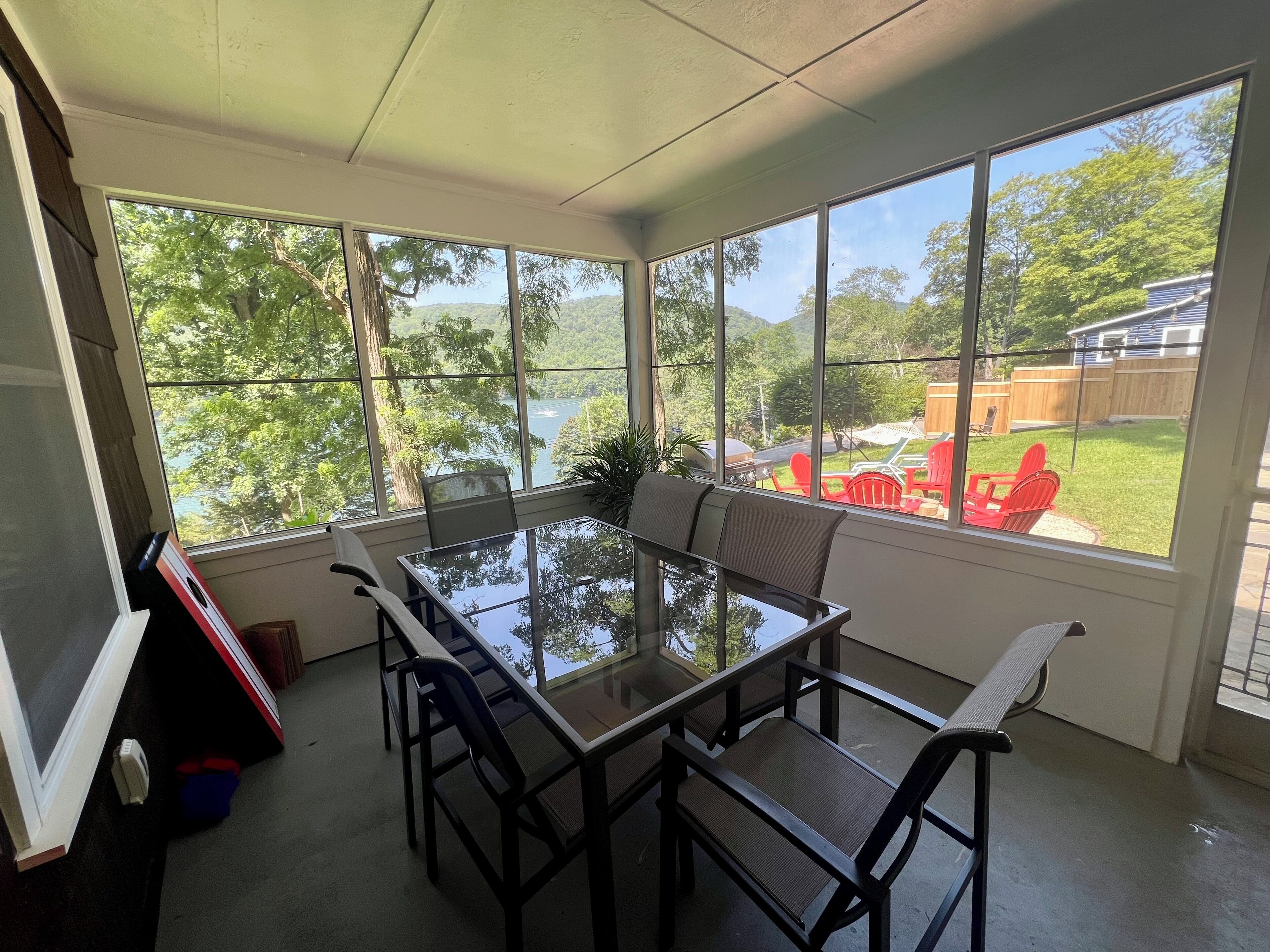 Un solárium con una mesa y sillas de vidrio, ventanas amplias y vistas a un patio trasero con zona de barbacoa.