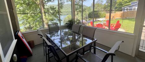 Un solárium con una mesa y sillas de vidrio, ventanas amplias y vistas a un patio trasero con zona de barbacoa.