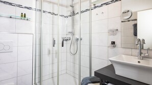 Un baño moderno con ducha de vidrio, un lavamanos blanco y un espejo encima.