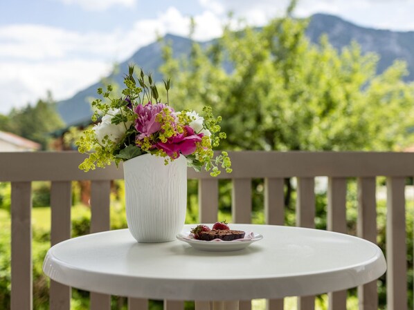 A white table with a vase of flowers and a plate of food on a balcony.