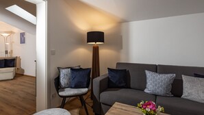 A modern living room with a grey sofa, a round ottoman, a wooden coffee table with a vase of flowers, and a tall floor lamp.