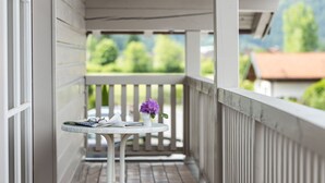 A balcony with a small table, a vase with flowers, and a view of greenery and buildings.