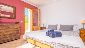Een slaapkamer met een bed, een dressoir, een spiegel en een deur naar een balkon.