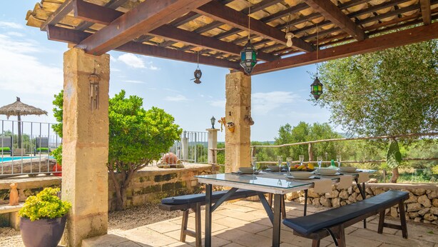 An outdoor patio with a table and benches, surrounded by stone walls and greenery.