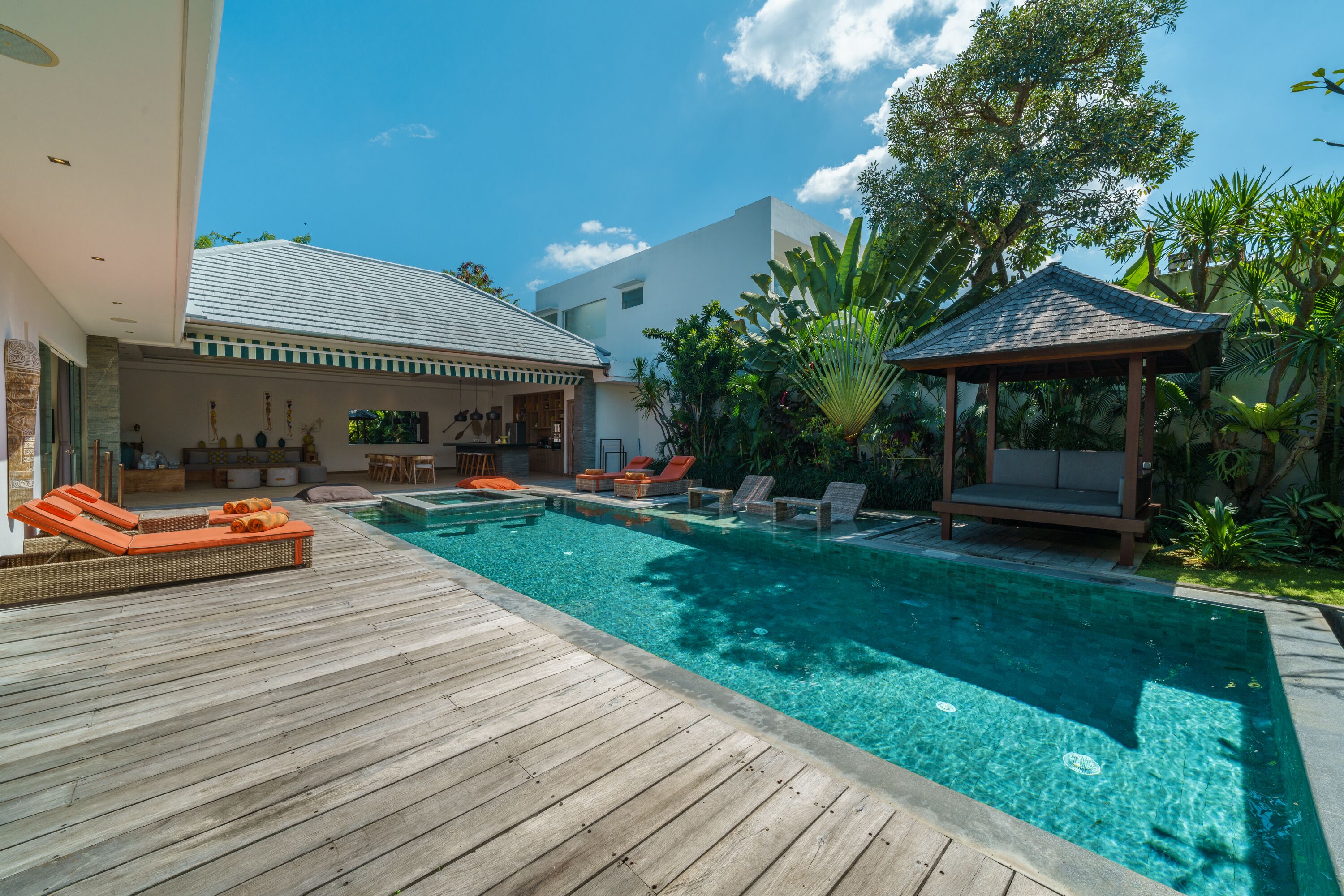 A wooden deck with a swimming pool, lounge chairs, and a gazebo.