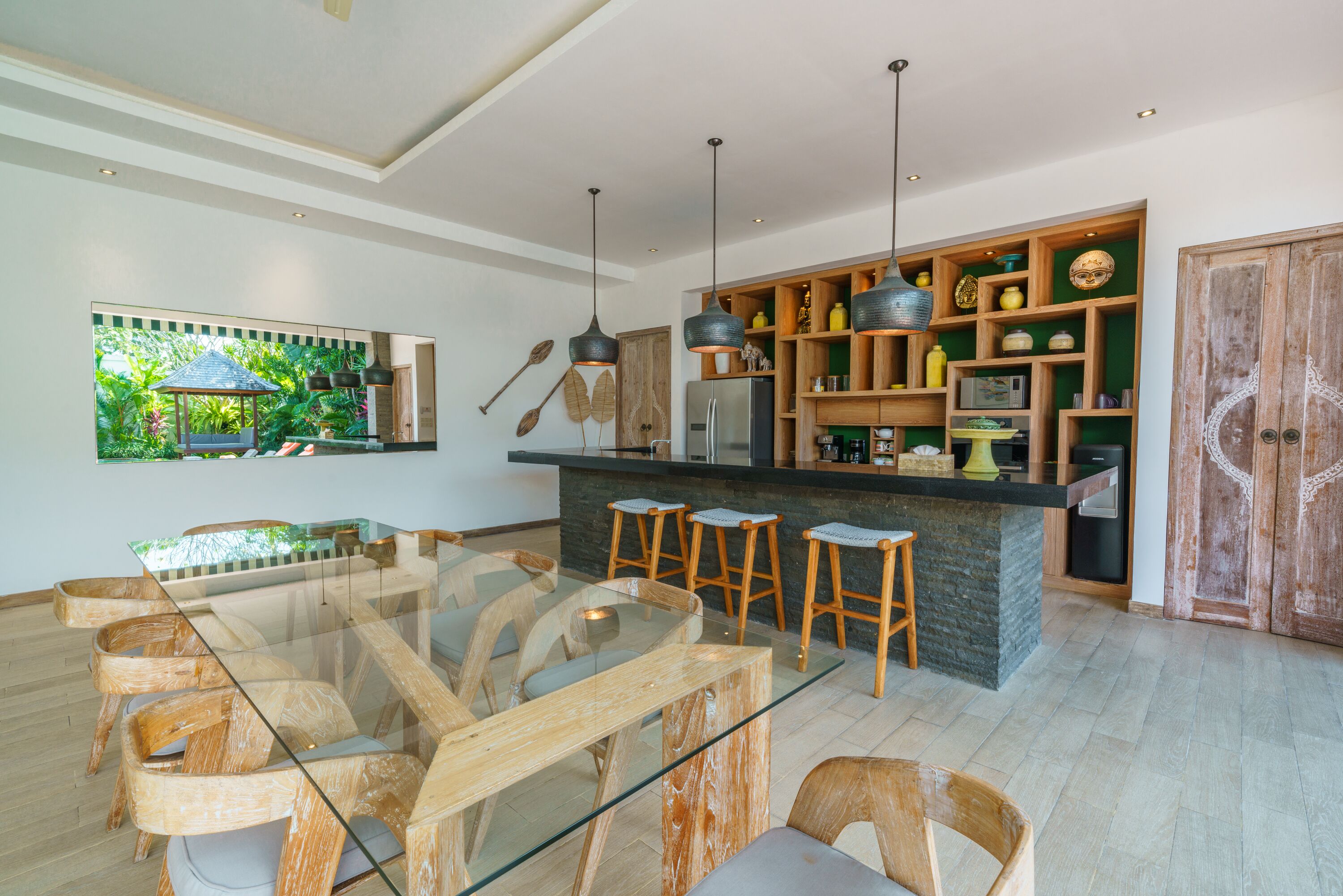 A modern kitchen with a glass dining table, wooden stools, and a built-in bar area.