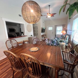 Un coin repas avec une table et des chaises en bois, un ventilateur de plafond, une cuisine équipée d’un four à micro-ondes et un salon avec un canapé et un téléviseur.