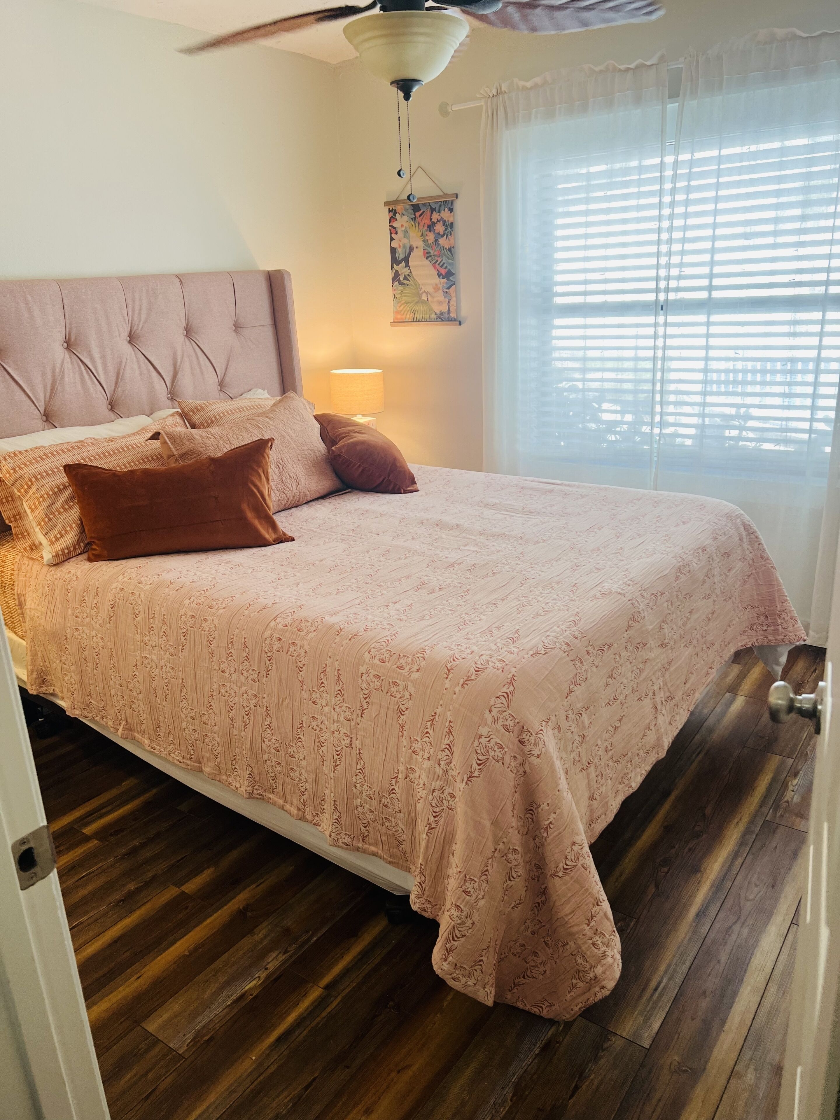 A bedroom with a tufted headboard, a floral-patterned bedspread, and a ceiling fan.