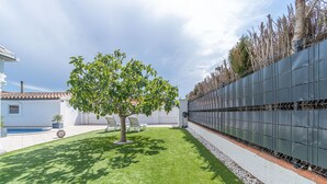 Un patio trasero bien cuidado, con un árbol, una piscina y una cerca blanca.