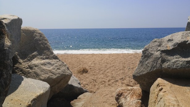 A beach with large rocks in the foreground and a clear view of the ocean.