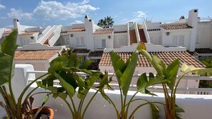 A residential area with white buildings and terracotta roofs, featuring balconies and potted plants.