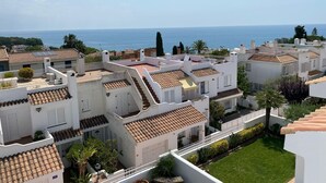 A residential area with white buildings, terracotta roofs, and a view of the sea.