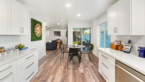 A modern kitchen with white cabinets, a wooden floor, and a dining area with a table and chairs. - Cozy 3BR Stadium Oasis! Pool + Hot Tub + Fire Pit (Glendale)
