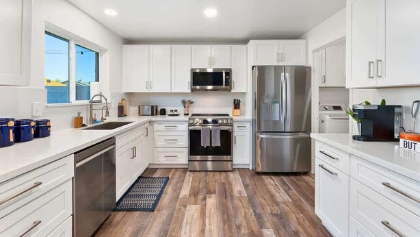 A modern kitchen with white cabinets, stainless steel appliances, and a wooden floor. - Cozy 3BR Stadium Oasis! Pool + Hot Tub + Fire Pit (Glendale)