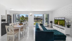 Una sala de estar moderna con un sofá color turquesa, un comedor con sillas blancas, una cocina con refrigerador y un televisor en la pared.