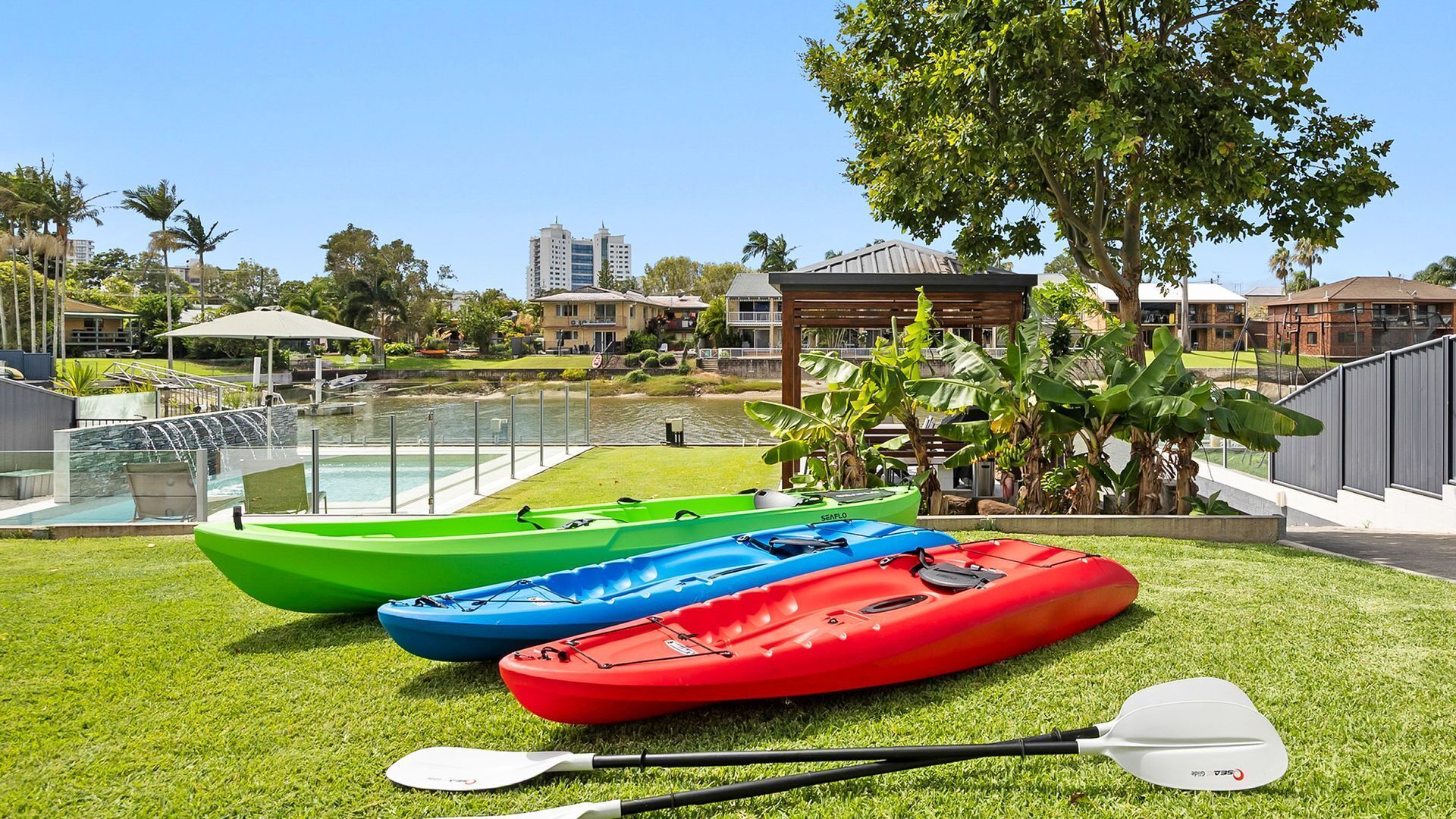 A grassy area with kayaks and a paddle, a pool, and buildings in the background.