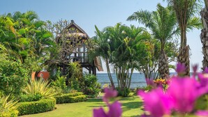 Un resort tropicale con una struttura a tetto di paglia, vegetazione lussureggiante e vista sul mare.