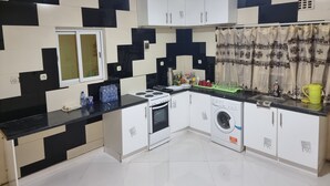 A kitchen with black and white checkered walls, a stove, oven, washing machine, and a window with a curtain. - Villa Sleeps 10 with Garden (DR Congo)