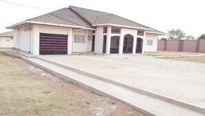 A two-story house with a tiled roof, a garage with a red door, and a concrete driveway. - Villa Sleeps 10 with Garden (DR Congo)