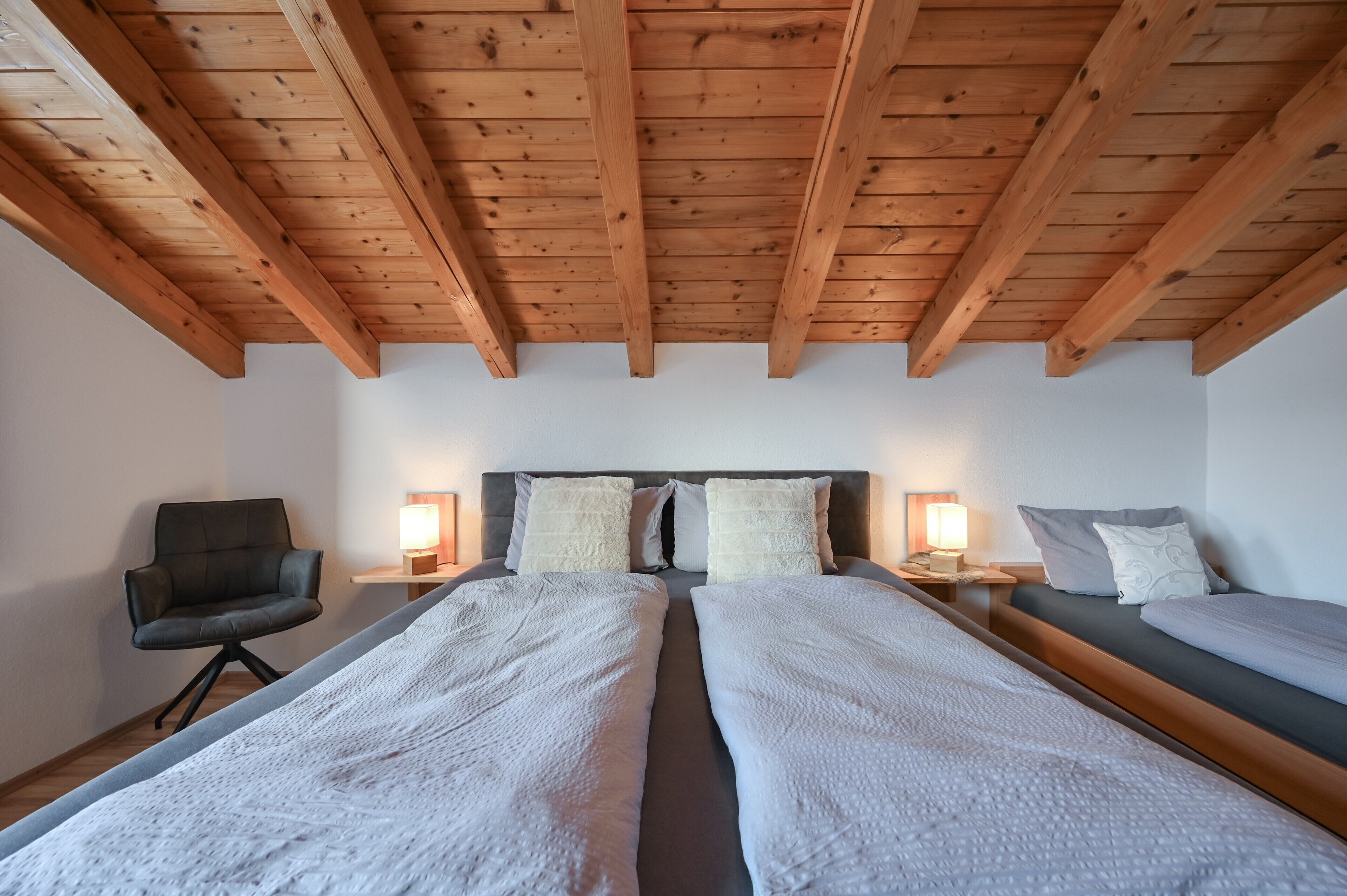 Una stanza con due letti, travi a vista in legno, una poltrona, lampade da comodino e un tavolino di servizio.
