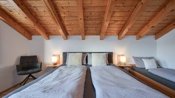 Una stanza con due letti, travi a vista in legno, una poltrona, lampade da comodino e un tavolino di servizio.