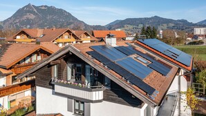 Un immeuble résidentiel doté d’un toit en pente, de panneaux solaires et d’un balcon agrémenté de fleurs.