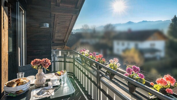 Un balcon avec une table préparée pour le petit-déjeuner, des plantes en pot et une vue sur les montagnes.