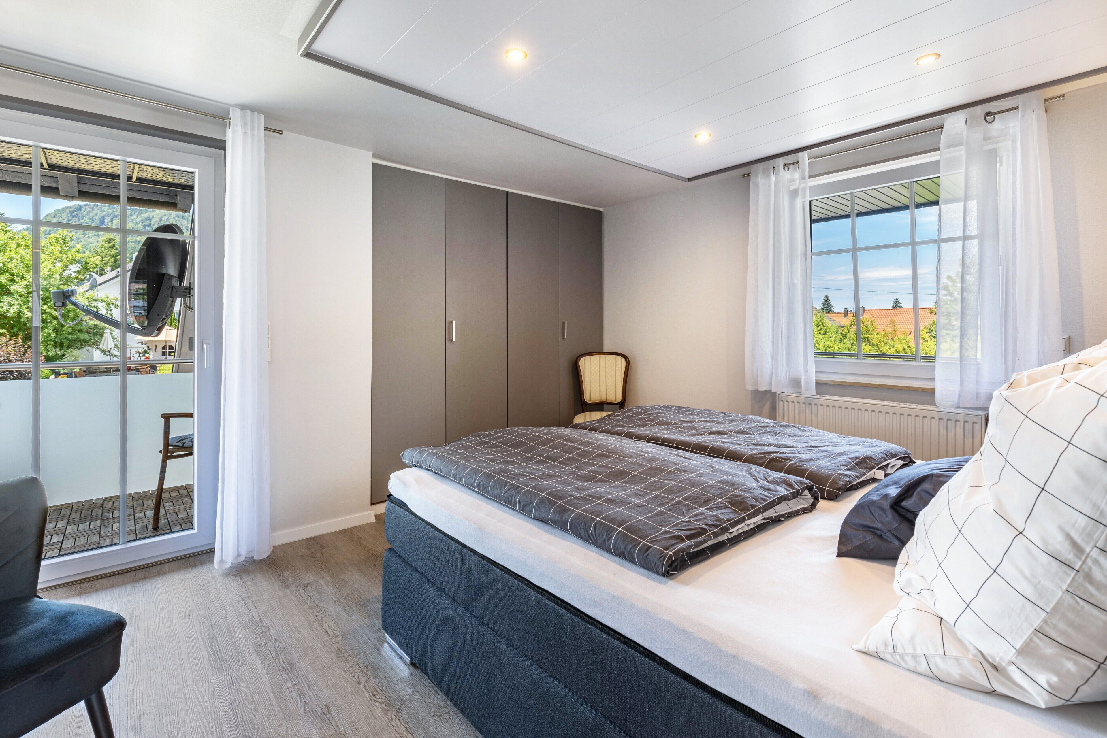 A bedroom with a bed, a chair, a wardrobe, and a window with a view.