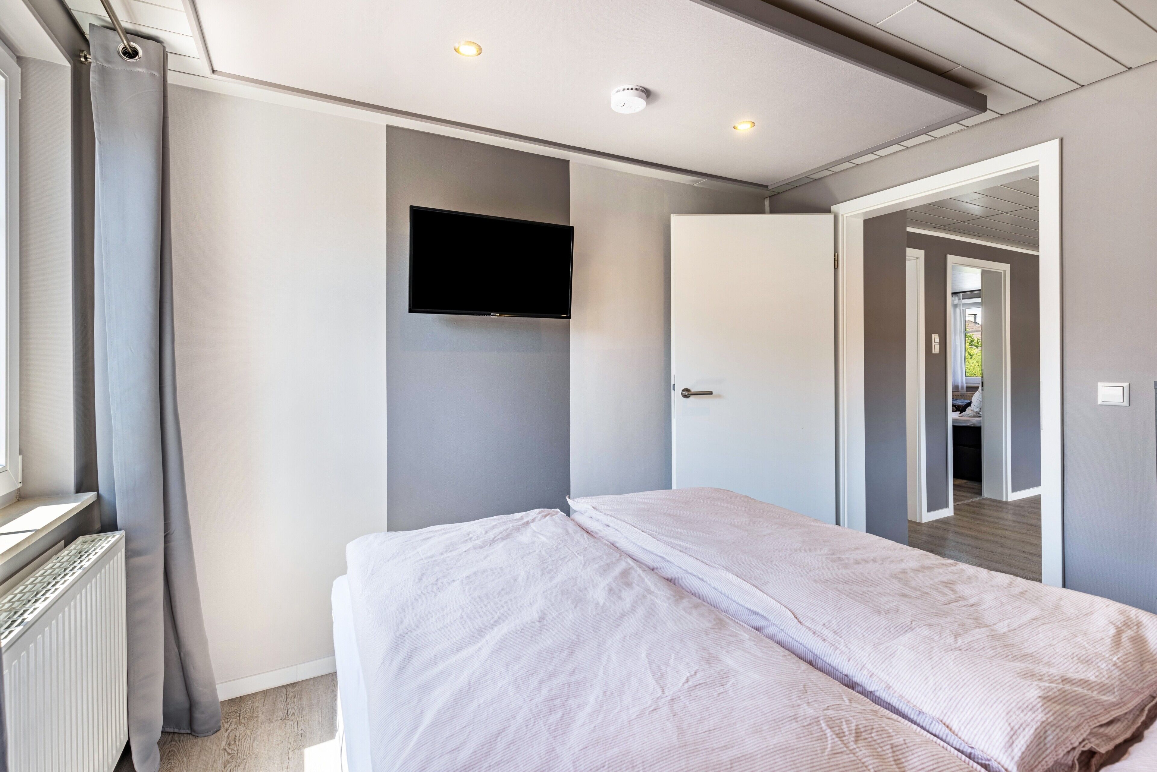 Een slaapkamer met een bed, een aan de muur bevestigde televisie en een deur naar een andere kamer.