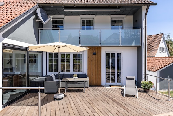 Ein modernes, zweistöckiges Haus mit Balkon, einem Essbereich mit Tisch und Stühlen sowie einem großen Fenster.