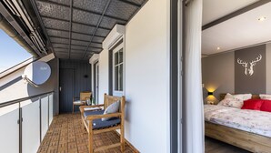 Ein Balkon mit Holzboden, einem Stuhl, einem Tisch und einem Bett mit blumigem Überwurf sowie einer Dekoration mit Hirschgeweih an der Wand.