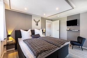 Ein modernes Schlafzimmer mit einem großen Bett, Nachttischen, einem an der Wand montierten Fernseher und einer Dekoration mit einem Hirschkopf.