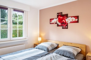 Une chambre à coucher avec un lit, une fenêtre, une table de chevet et une œuvre d’art accrochée au mur.