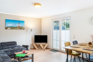 A living room with a flat-screen TV, a sofa, a coffee table, and a dining area with chairs and a table.